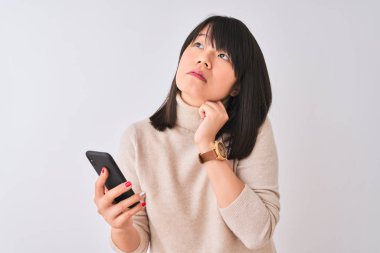 Genç güzel Çinli kadın izole beyaz arka plan üzerinde duran akıllı telefon kullanarak soru hakkında ciddi yüz düşünme, çok karışık bir fikir