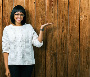 Güzel genç Afro-Amerikan kadın neşeli sunulması ve kameraya bakarak avucunun ile işaret gülümseyen izole arka plan üzerinde gözlük.