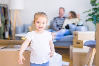 Güzel aile, anne-babalar kanepede kahve içme oturmuş karton kutular etrafında yeni evde oynayan çocuğuna bakıyor