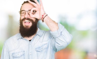 Uzun saç ve sakal gülümseyen, parmakları ile mutlu yüz üzerinden seyir göz el ile ok jest yapıyor gözlüklü genç hipster adamla.