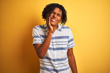 Dreadlocks izole sarı arka plan üzerinde diş ağrısı veya diş üzerinde diş hastalığı nedeniyle ağrılı ifade ile el ile ağız dokunmadan çizgili gömlek giyen Afro Amerikan adam. Diş hekimi konsepti.