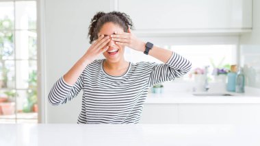 Afro saçlı güzel afro-amerikan kadın rahat çizgili kazak elleri ile gözleri kaplayan giyen neşeli ve komik gülümseyen. Kör kavramı.