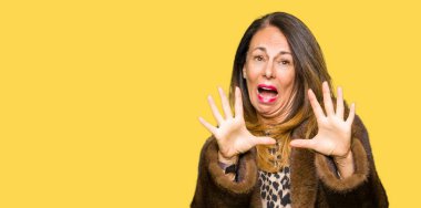 Şokta bağırarak korkuyor ve korku ifade dur hareketi el ile ile dehşete vizon kürk giyen güzel orta yaş zarif kadın. Panik kavramı.