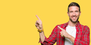 Yakışıklı adam gülümseyen ve kamera iki el ve parmak tarafına işaret görünümlü rahat gömlek giyiyor.