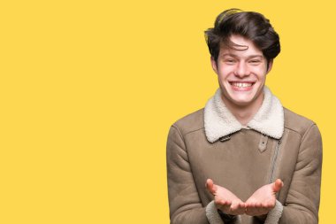 Genç yakışıklı adam giyen kış ceket izole üzerinden alma veya jest vererek birlikte el avuç içi ile gülen arka plan. Ayrı tutma ve koruma