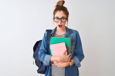 Izole beyaz arka plan üzerinde kitap tutan sırt çantası giyen Redhead öğrenci kadın sürpriz bir yüz ile şok korkmuş, korku ifade korku ve heyecanlı