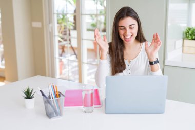 Güzel genç öğrenci kadın dizüstü bilgisayar ve dizüstü bilgisayar kullanarak üniversite için okuyan çok mutlu ve heyecanlı, kazanan ifade büyük bir gülümseme ile çığlık zafer kutluyor ve ellerini kaldırdı