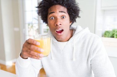 Afro-Amerikan adam tutan ve portakal suyu bardak içme sürpriz bir yüz ile şok korkmuş, korku ifade korku ve heyecanlı