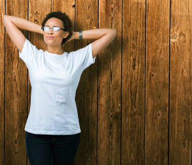 Güzel genç Afro-Amerikan kadın gözlük izole üzerinde arka plan dinlenirken ve germe kollar ve eller baş ve boyun arkasında ile mutlu gülümseyerek