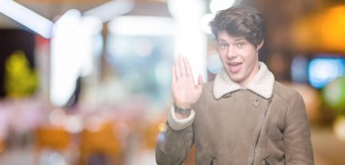 Yakışıklı delikanlı izole arka plan Waiving mutlu selam söyleyerek üzerinde kış ceket ve gülümseyen, dostça karşılama jest