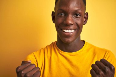 Izole sarı arka plan üzerinde duran rahat t-shirt giyen Afro-Amerikan adam gurur çığlık ve zafer ve başarı çok heyecanlı kutluyor, duygu tezahürat