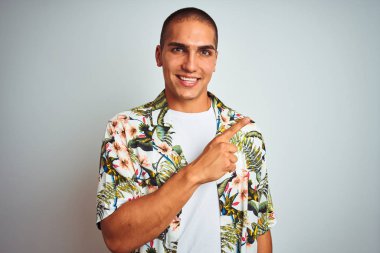 Genç yakışıklı adam beyaz arka plan üzerinde Hawaii gömlek giyen yüzünde mutlu ve doğal ifade ile yan yana el ve parmak ile işaret eden yüz bir gülümseme ile neşeli