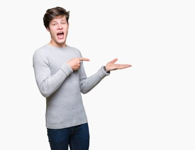 Hayret ve el ile sunulması ve parmak ile işaret ederken kameraya gülümseyen izole arka plan üzerinde kış kazak giyen genç yakışıklı adam.