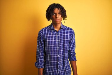 Yalnız sarı arka plan şüpheci ve sinir üzerinde duran rahat gömlek giyen dreadlocks ile Afro adam, sorun nedeniyle üzgün kaşlarını çatma. Negatif kişi.