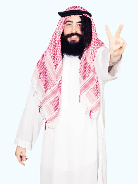 アラビア ビジネスの男性と伝統的なクーフィーヤ スカーフ表示と指番号のいずれかニコニコしながら自信を持って 幸せに上向きを身に着けている長い髪 — ストック写真