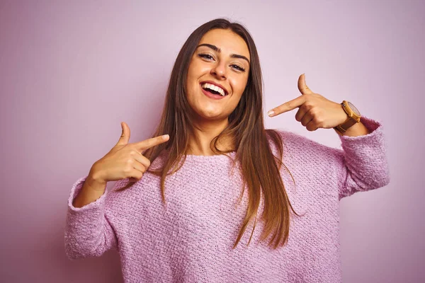 カジュアルなセーターを着た若い美しい女性は 孤立したピンクの背景の上に立って陽気な笑顔を見せ 指の歯と口で指差します 歯科健康の概念 — ストック写真
