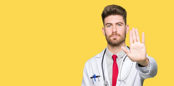 若いハンサムな医者の手の手のひらで停止歌ってをして医療のコートを着た男 顔に否定的な深刻なジェスチャーで警告式 — ストック写真