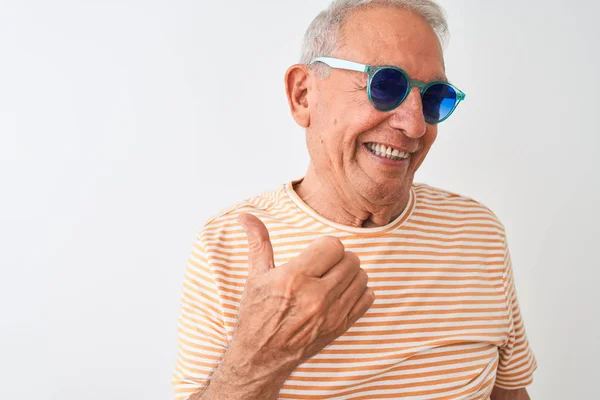 穿着条纹T恤和太阳镜的白发老人在孤立的白色背景上微笑着 脸上露出幸福的表情 竖起大拇指指着一边 — 图库照片