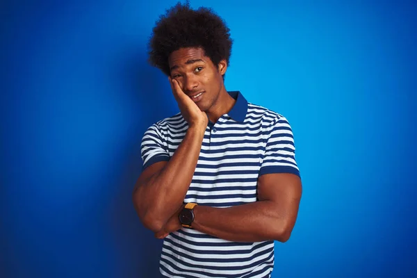 African american man with afro hair wearing striped polo standing over isolated blue background thinking looking tired and bored with depression problems with crossed arms.