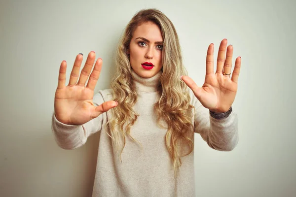 Beautiful woman wearing winter turtleneck sweater over isolated white background doing stop gesture with hands palms, angry and frustration expression
