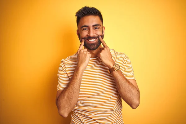 孤立した黄色の背景の上に立つTシャツを着た若いインド人男性が口を開き 指を指差し 明るい笑顔を強いられる — ストック写真