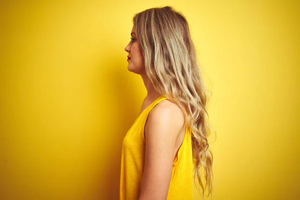 黄色の孤立した背景の上に立つTシャツを着た若い美しい女性が横を向き 自信満々の笑顔で自然な顔でプロフィールポーズをリラックス — ストック写真