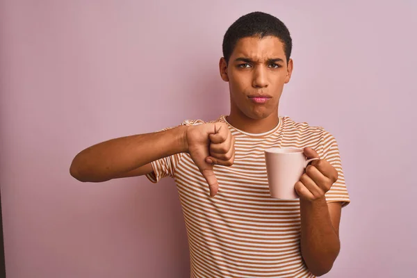 Handsome arab man wearing striped t-shirt drinking coffee over isolated pink background with angry face, negative sign showing dislike with thumbs down, rejection concept