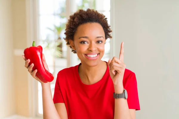 年轻的非洲裔美国妇女拿着新鲜的红辣椒惊讶与一个想法或问题指向手指与快乐的脸 — 图库照片