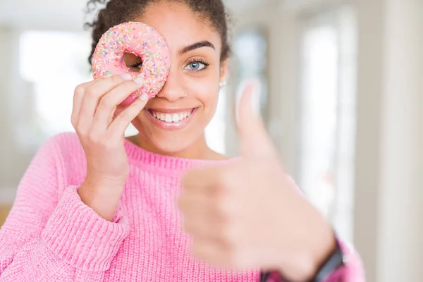 甘いピンクのドーナツを食べる若いアフリカ系アメリカ人の女の子は Okサインをやって大きな笑顔で幸せ 指で親指 優れた兆候 — ストック写真