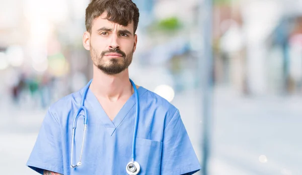 Young handsome nurse man wearing surgeon uniform over isolated background depressed and worry for distress, crying angry and afraid. Sad expression.