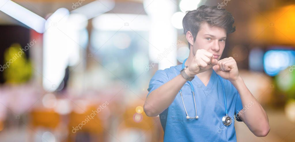 Young doctor wearing medical uniform over isolated background Punching fist to fight, aggressive and angry attack, threat and violence