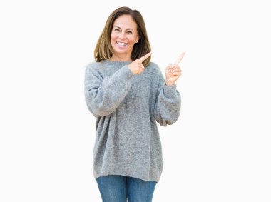 Gülümseyen ve iki elleri ve parmakları ile tarafına işaret kamera bakarak izole arka plan üzerinde kış kazak giyen güzel orta yaş kadın.