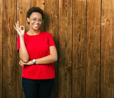 İzole arka plan el ve parmaklar ok işaretiyle yapıyor olumlu gülümseyen üzerinde gözlük güzel genç Afro-Amerikan kadın. Başarılı ifade.