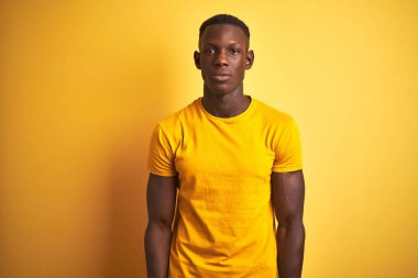 Izole sarı arka plan üzerinde duran rahat t-shirt giyen genç Afro-Amerikan adam yüzünde ciddi ifade ile rahat. Kameraya basit ve doğal bir bakış.