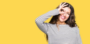 El gülümseyen ok jest yapıyor çizgili kazak giyen genç güzel kadın, göz mutlu yüz ile parmaklara bakarak.