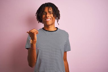 Dreadlocks giyen dreadlocks ile afro adam izole pembe arka plan üzerinde duran mutlu yüz görünümlü ve başparmak ile yan işaret.