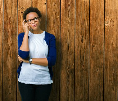 Genç güzel Afrikalı-Amerikalı kadın gözlük ile izole arka plan üzerinde çene düşünme hakkında soru, dalgın ifade ver. Düşünceli yüzüyle gülümsüyor. Şüphe kavramı.