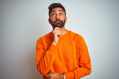 Izole beyaz arka plan üzerinde turuncu kazak giyen genç hintli adam çenesi üzerinde el ile soru, dalgın ifade düşünme. Düşünceli bir yüzle gülümsüyor. Şüphe kavramı.