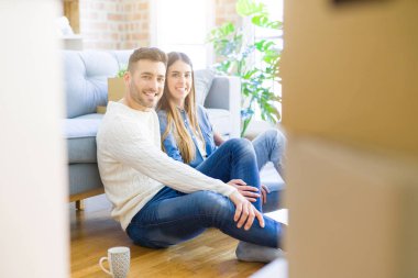 Yeni bir daire zemin üzerinde oturan genç güzel çift, yeni bir eve taşınmak için mutlu sevgi gülümsüyor