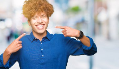 Afro saçlı genç yakışıklı zarif adam emin gösteren gülümseyen ve parmakları diş ve ağız ile işaret. Sağlık kavramı.