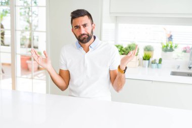 Yakışıklı İspanyol adam evde rahat beyaz t-shirt silah ve elleri kaldırdı ile clueless ve karışık ifade. Şüphe kavramı.