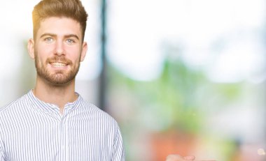 Genç yakışıklı adam neşeli sunma gülümseyen ve kamera bakarak el avuç ile işaret.