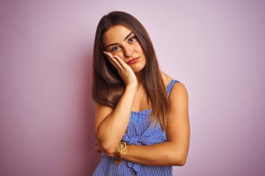 İzole pembe arka plan üzerinde duran çizgili elbise giyen genç güzel kadın yorgun görünümlü ve çapraz kolları ile depresyon sorunları ile sıkılmış düşünme.