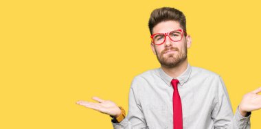 Gözlük clueless ve şaşkın bir ifadeyle kollar ve eller kaldırdı giyen genç yakışıklı iş adam. Şüphe kavramı.