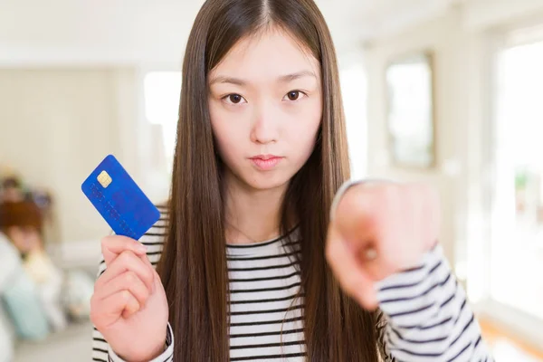 Beautiful Asian woman holding credit card pointing with finger to the camera and to you, hand sign, positive and confident gesture from the front