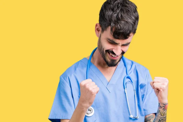 Young handsome nurse man wearing surgeon uniform over isolated background very happy and excited doing winner gesture with arms raised, smiling and screaming for success. Celebration concept.