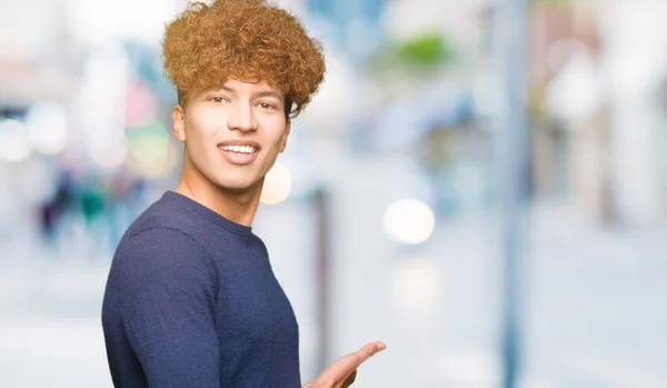 Young handsome man with afro hair Inviting to enter smiling natural with open hand