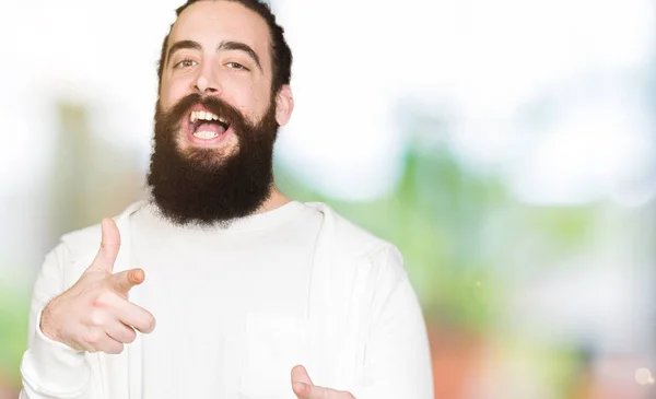 Young man with long hair and beard wearing sporty sweatshirt pointing fingers to camera with happy and funny face. Good energy and vibes.