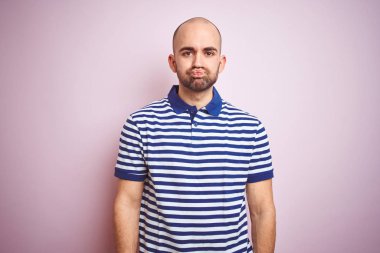 Komik yüzü ile pembe izole arka plan üzerinde rahat çizgili mavi t-shirt giyen sakallı genç kel adam yanakları şişirme. Ağız hava ile şişirilmiş, deli ifade.