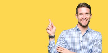 Yüzünde kocaman bir gülümseme ile mavi gözlü yakışıklı iş adamı kameraya bakarak yan el ve parmak ile işaret.